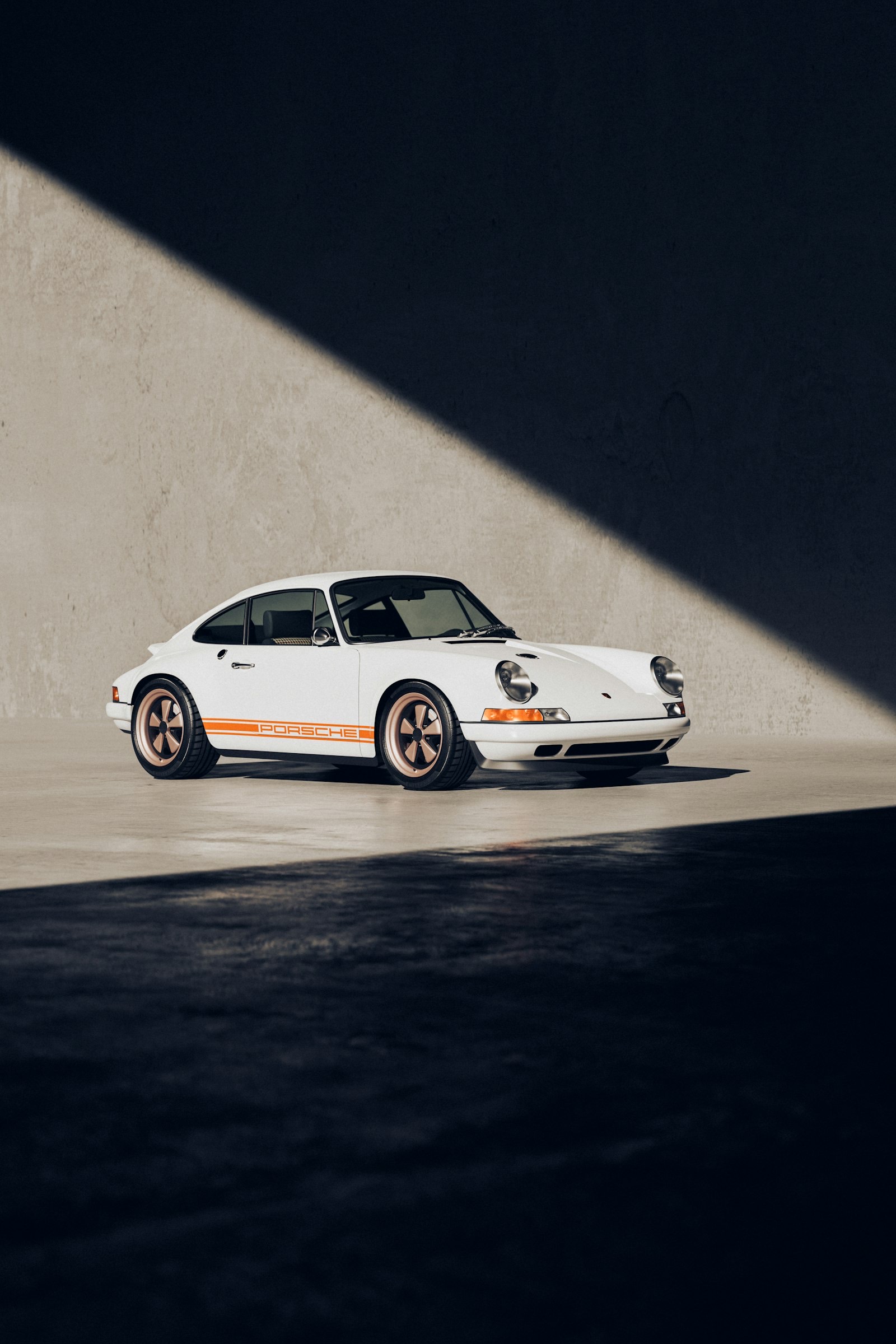White backdated Porsche 911 restomod with orange livery, parked in dramatic side light