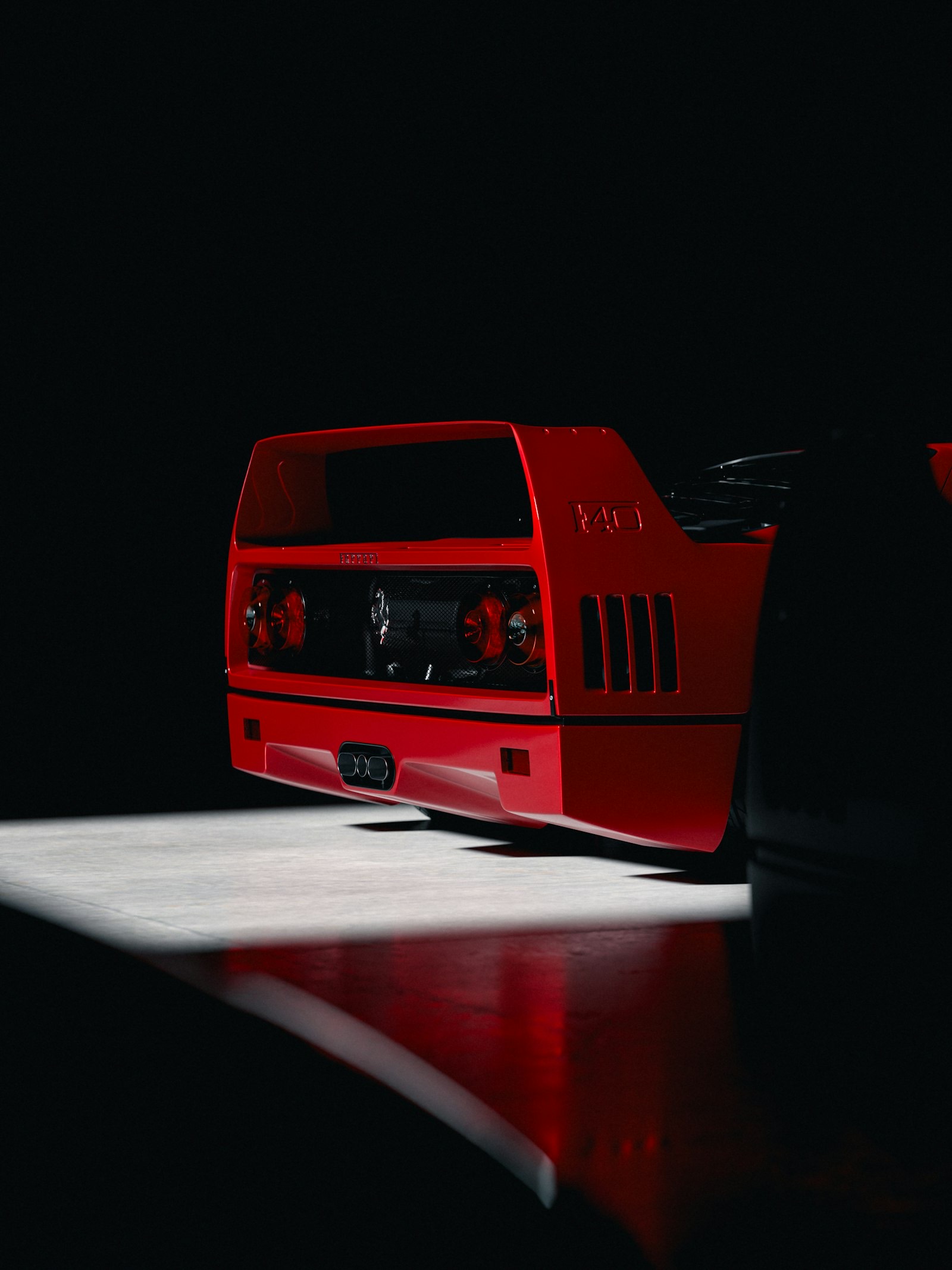 Rear of a red Ferrari F40 emerging from shadow in studio lighting