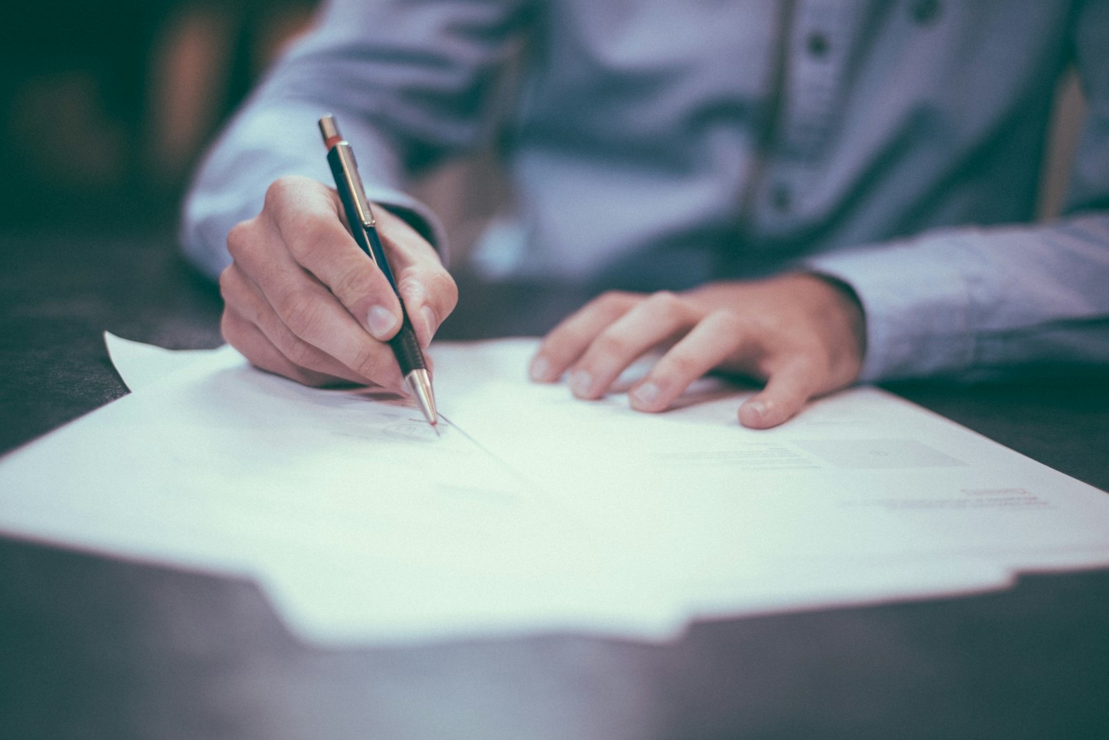 Hands signing paperwork at a desk with a pen