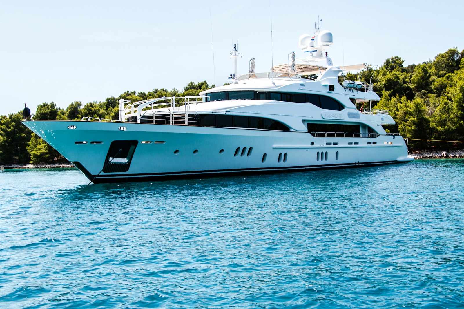 White superyacht anchored off a wooded coastline